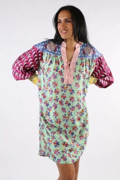 Tie placket long sleeve dress with wide cuffs in our Twisted Love print. Each piece of the dress is a different, colorful pattern. The packet is pink, with roses on both sides at the top. Sleeves are puffed in pink and purple zigzag stripes with wide yell