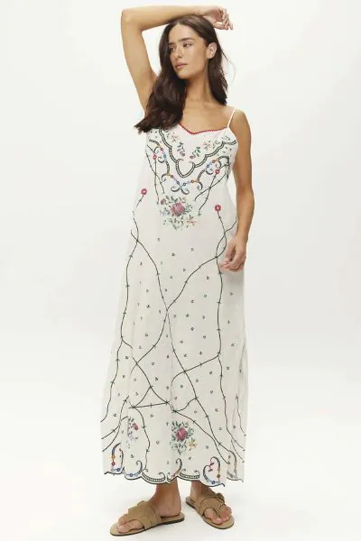 Pure romance in white linen. The Lauren slip dress features delicate floral embroidery inspired by antique hand stitch patterns, with trailing vines creating an elegant lattice across the fabric. Vibrant blooms cluster at the neckline and hemline, 